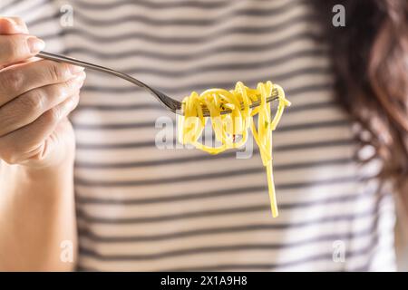 Young woman enjoys eating spaghetti. He has Aglio e Olio pasta twisted on his fork. Close up. Stock Photo