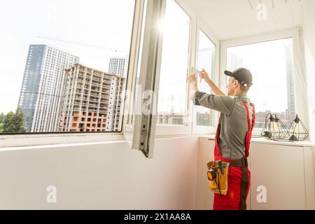 Maintenance man is fixing windows in a living room using a skrewdriver. He is wearing glasses, yellow gloves and a black apron Stock Photo