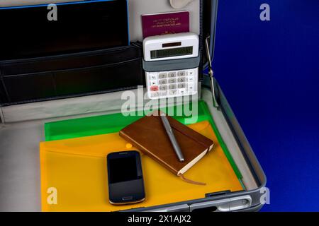 Closeup view of briefcase with tablet notebook pen mobile phone calculator and files on a blue desk top Stock Photo