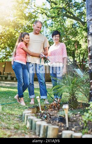 Family, bonding and watering plants in backyard garden for sustainability, environmental or agriculture. Landscaping, mature parents and young girl in Stock Photo