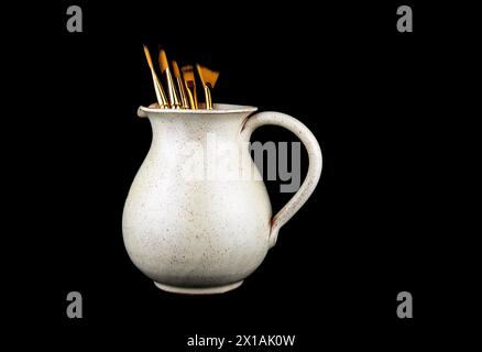 Old earthenware wine jug with assorted artists paint brushes isolated on a black background Stock Photo