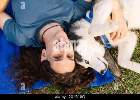 Horizontal photo a man and his husky playfully lie upside down on the grass, sharing a unique perspective and a joyful connection in the gre Stock Photo