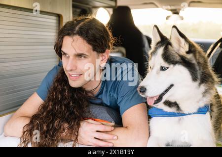 Horizontal photo a man with luscious curly hair shares a relaxed moment with his joyful husky inside the comfortable space of their modern c Stock Photo