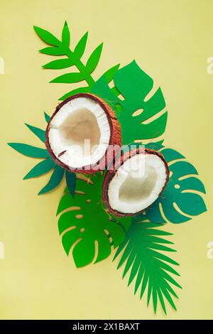 Broken coconut and paper tropical leaves on a light yellow background. Summer background, flat lay. Stock Photo