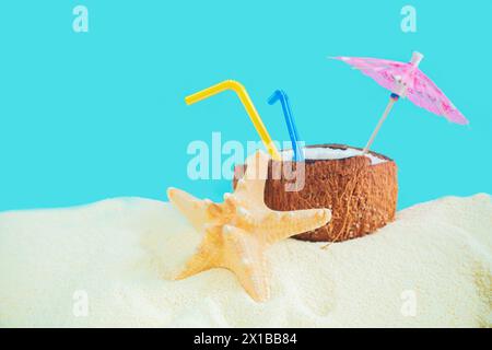 Coconut with a straw, shells, starfish and a sun umbrella on the sand. Summer background, concept of relaxation and vacation. Stock Photo