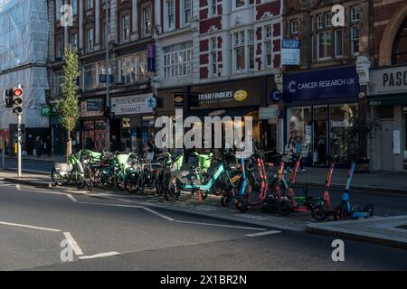 Electric bicycles ands scooters await fares in London's Kensington High Street. Stock Photo