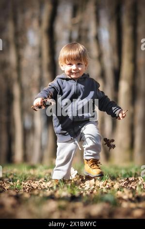 Toddlers autumn adventure. Curious kid crouches among fallen leaves, discovering the wonders of nature. Child playing outdoors Stock Photo