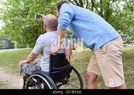 A person using a wheelchair and a standing person enjoying time together in nature, capturing a selfie moment. Stock Photo
