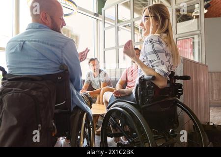 A diverse group of individuals including persons using wheelchairs having a conversation in a well-lit indoor space, showcasing inclusion and accessib Stock Photo