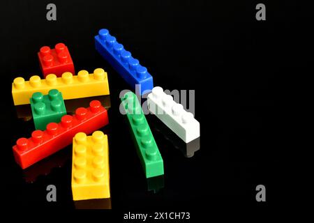 Multi-colored plastic parts of the designer randomly lie on a black background. Stock Photo