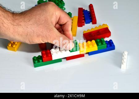 A man's hand holds a piece of the designer in his fingers and tries to install it on an already assembled structure from the details of a children's c Stock Photo