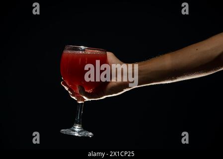 A right hand holding a glass cup with guava juice inside. Isolated on dark background. Stock Photo