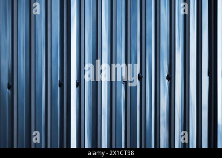 Shiny blue ridged metal fence connected with bolts and nuts, close up abstract background photo with selective soft focus Stock Photo