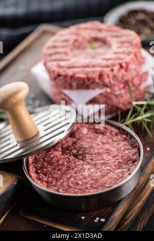 Fresh raw ground beef patties with rosemary salt and pepper made in a meat form on a cutting board. Stock Photo
