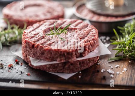 Fresh raw ground beef patties with rosemary salt and pepper made in a meat form on a cutting board. Stock Photo