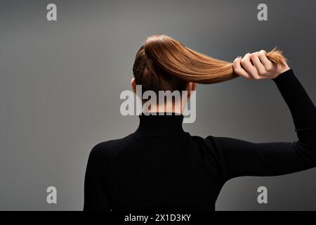 Back view of young stylish woman with long hair elegantly styled in a ponytail, exuding grace and confidence. Stock Photo