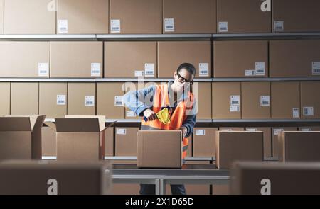 Bored warehouse worker sealing boxes on the conveyor belt with adhesive tape Stock Photo