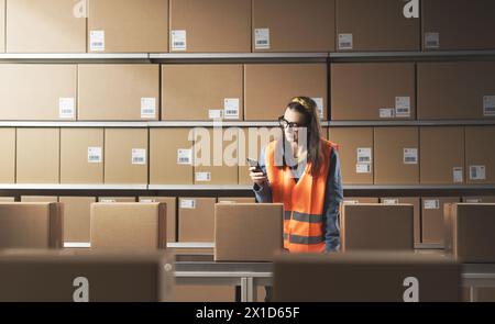 Bored distracted female warehouse worker using her smartphone at work Stock Photo