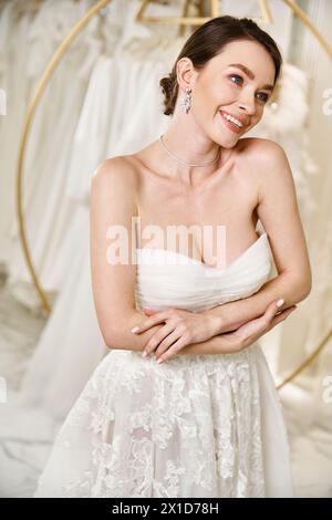 A beautiful young brunette bride in a white wedding dress poses gracefully for a picture in a bridal salon. Stock Photo