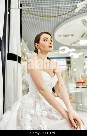 A young brunette bride in a flowing white dress sits elegantly on a ...