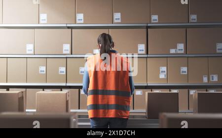 Female warehouse worker checking boxes on the conveyor belt, back view Stock Photo