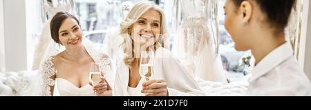 A young bride in a wedding dress raises her champagne flute with her two bridesmaids in a bridal salon. Stock Photo