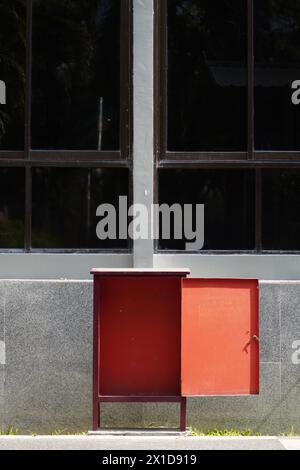 An open red iron box with a black window and gray walls as a background Stock Photo