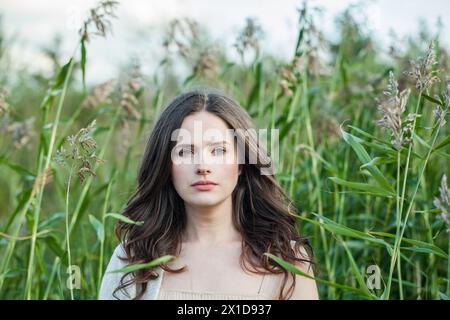One healthy young brunette woman with fresh clear skin and long dark brown hair outdoors on green grass background, air portrait Stock Photo