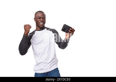 young positive african man dressed in a spring jacket feels joy holding a smartphone Stock Photo