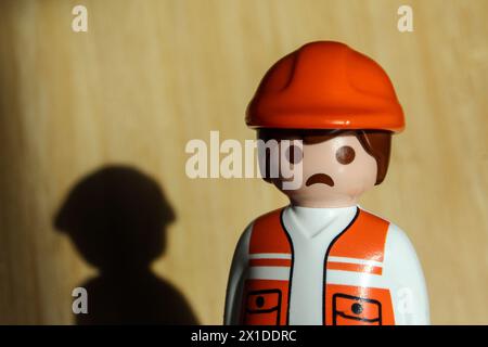 Playmobil toy worker figure, with with a grimace of sadness and its shadow reflected in the background Stock Photo