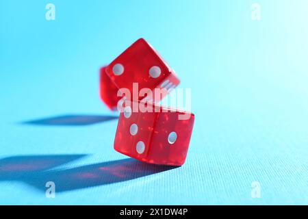 Three red game dices falling on light blue background, closeup Stock Photo