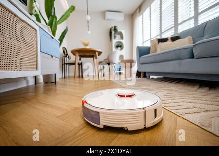 Robotic vacuum cleaner cleaning wooden floor in living room Stock Photo
