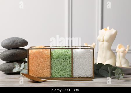 Different types of sea salt, spoon, spa stones, candles and eucalyptus branches on wooden table Stock Photo