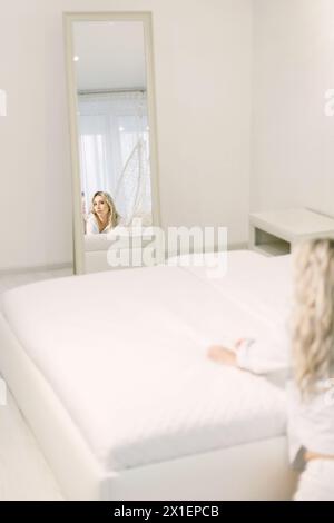 A woman is holding a smartphone, taking a picture of herself reflected in a mirror. Stock Photo