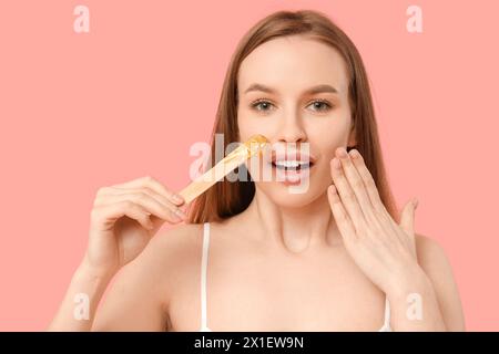 Beautiful young shocked woman holding spatula with sugaring paste on pink background Stock Photo