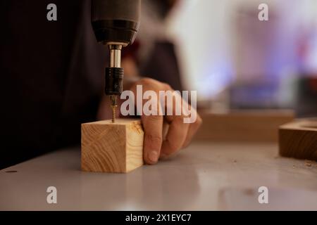 Woodworker in assembly shop using power drill to create holes for dowels in wooden board. Carpenter sinking screws into wooden surfaces with electric tool, doing precise drilling for seamless joinery Stock Photo