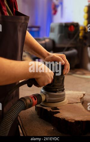 Manufacturer using angle grinder on lumber block to smooth surfaces by abrasion with sandpaper. Man using orbital sander gear for furniture assembling job in assembly shop Stock Photo