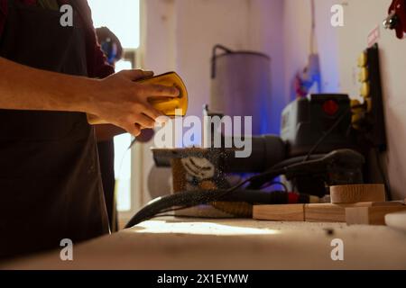 Woodworker working in carpentry shop using sanding block to remove imperfections on wood piece. Carpenter using coarse grade sandpaper to do manual sanding, close up shot Stock Photo