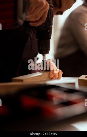 Manufacturer in carpentry shop using power drill to create holes for dowels in wooden board. Woodworking expert sinking screws into wooden surfaces with electric tool, doing precise drilling Stock Photo