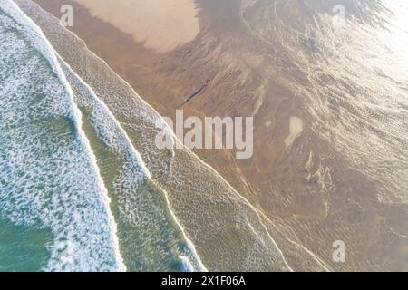 zenithal aerial view of two people walking along the shore of an empty beach in summer at sunrise. Drone shot Stock Photo
