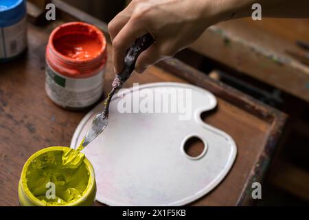 Top view of colored acrylic paint pots, plastic palette and palette knife used for painting in the art studio. Space for copying. Concept of artist an Stock Photo