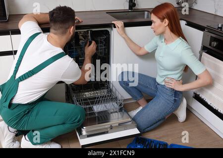 Woman looking how serviceman repairing her dishwasher in kitchen Stock Photo
