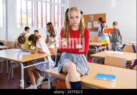 Sad bored girl sitting separately in classroom in break between lessons Stock Photo