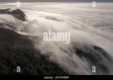 The sky is covered in a thick layer of fog, creating a moody and mysterious atmosphere. The misty clouds hang low over the mountains, giving the scene Stock Photo