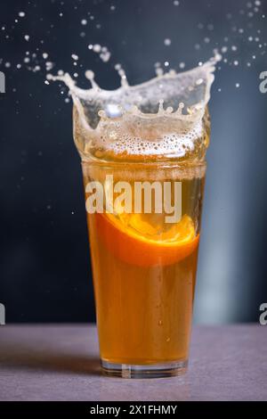 A glass of beer with an orange slice in it splashing out of the glass Stock Photo