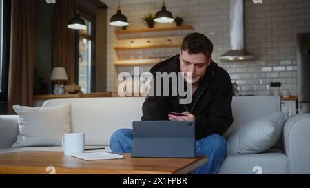 Man sit on sofa at home entering credit card number on tablet computer for shop online credit card is declined or out of limit, feeling angry and unha Stock Photo