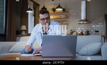 Professional young doctor with glasses wear white uniform with stethoscope having online conference video call with patient through into laptop webcam Stock Photo