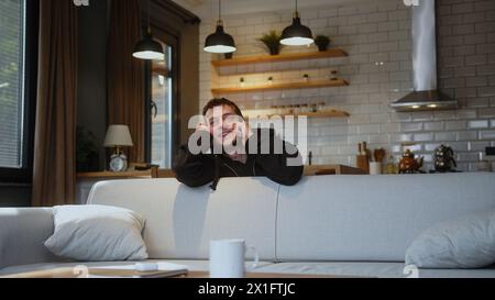 Happy man in love leaning over the back of the sofa while talking on mobile phone with his girlfriend enjoying the conversation, spending leisure time Stock Photo