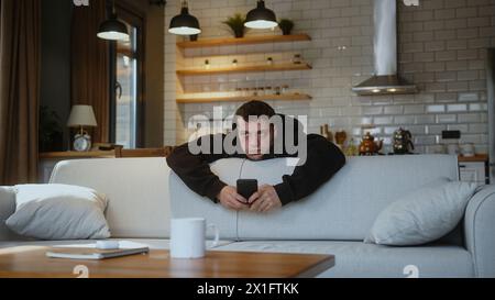 Man leaning over the back of the sofa feeling bored, suffering from depression. Stock Photo