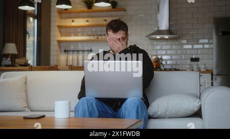 Frustrated man sit on sofa at home entering credit card number on laptop for shop online credit card is declined or out of limit, feeling sad and unha Stock Photo